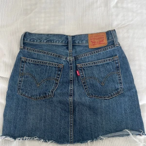 Levi's jeanskjol, W26, strl 26 - Snygg jeanskjol från Levi's i klassisk blå denim, W26 Kjolen har fem fickor och tydliga kontrastsömmar. Sparsamt använda, superfint skick💕💕 Säljer en svart och en ljus denim också. Stor utrensning pga flytt, se profil