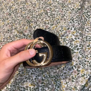 Svart Gucci skärp med guldspänne - Snyggt svart skärp från Gucci med ikoniskt GG-spänne i guld. Bältet är gjort i skinn och har diskret präglad logga längs hela bandet. Perfekt accessoar för att lyfta vilken outfit som helst.