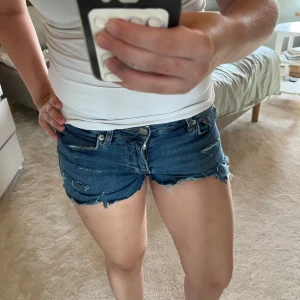 Blå lågmidjade jeansshorts  - Jätte fina blåa shorts med slitningar och småhål i sig. Själv klippt till shorts och gjort slitningar. Jätte sköna säljer pågrund av att dom inte kommer till användning 