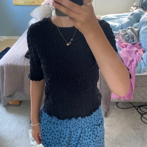 Svart strukturerad topp från Name It - Svart topp från Name It med coolt strukturerat tyg och lätt rynkade kanter. Modellen har trekvartsärm och en tight passform som sitter snyggt. Perfekt för dig som gillar en enkel men ändå unik stil.