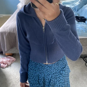 Blå croppad hoodie från Gina Tricot - Säljer en marinblå croppad hoodie från Gina Tricot med dragkedja framtill och huva. Tröjan har långa ärmar och bred ribbad mudd vid midjan och ärmsluten. Perfekt för dig som gillar en chill och trendig look.