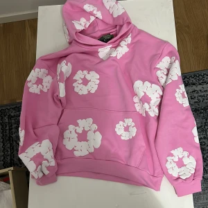 Rosa hoodie från Denim Tears S - Säljer en rosa hoodie från Denim Tears i 100% bomull med stora vita blommiga tryck över hela tröjan. Hoodien har huva och klassisk känguruficka framtill. Passar upp till 184cm
