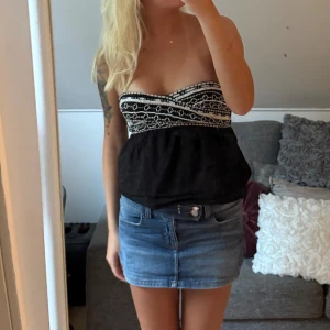 Svart bandeau tubtopp från Zara - Svart bandeau tubtopp från Zara med broderade vita detaljer upptill. Toppen är axelbandslös och har en lätt utställd passform nedtill. Perfekt för dig som vill ha en snygg och enkel topp med coola mönsterdetaljer.