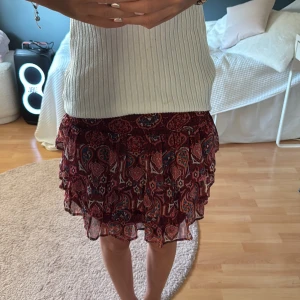 Röd volangkjol med mönster - Supersöt kort kjol i rött med  mönster i blått. Kjolen har flera volanger och resår i midjan för en bekväm passform, alltså väldigt stretchig. Jag skulle säga att den passar Xs/S