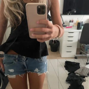 Levi's slitna jeansshorts låg midja - Säljer ett par blå jeansshorts från Levi's med låg midja och råa, fransiga kanter. Shortsen har slitna detaljer och klassiska fem fickor. Perfekta för sommaren och ger en avslappnad vibe.