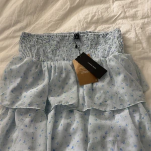 Ljusblå blommig volangkjol Vero Moda - Om du är intresserad skriv inann du köper! Helt ny Supersöt ljusblå kortkjol från Vero Moda med små blommor i blått och grönt. Kjolen har smock i midjan och flera volanger 