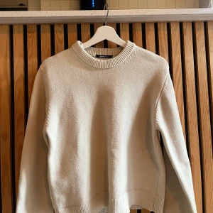 Beige stickad tröja från Gina Tricot - Säljer en beige stickad tröja från Gina Tricot i storlek XS. Tröjan har en rund halsringning med bred ribbad kant och långa ärmar. Perfekt för lager-på-lager och enkel att matcha med jeans eller kjol.