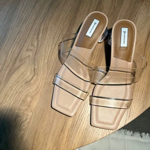 Genomskinliga slip-in sandaler, strl 41 - Trendiga klackar från Stradivarius. Storlek 41. Transparenta remmar i vinyl. Genomskinlig klack. Fyrkantig tå. 7 cm hög klack. 