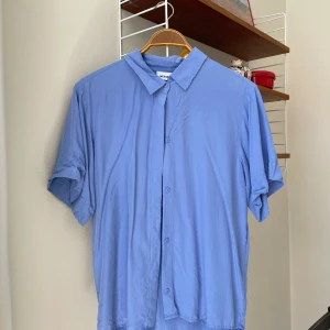 Kortärmad skjorta  - Skjorta från Weekday i vacker blå färg med lyster. 100 % modal. Strl 34. Fint skick!