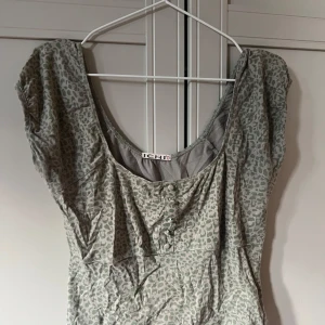 Y2k topp  - Snygg grå/grön topp från ICHI med leopardmönster och rundad urringning. Toppen har korta ärmar och knappar framtill som en extra detalj. Perfekt för dig som gillar djurmönster och vill sticka ut lite extra.