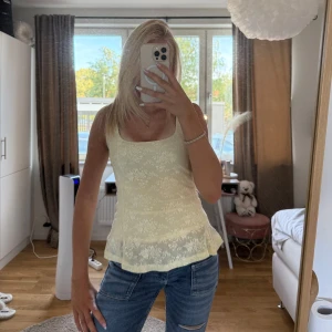 Ljusgul blommig linnetopp - Supersöt ljusgul linnetopp med blommigt mönster och volang nertill. Toppen är ärmlös och har en feminin, lätt utsvängd passform som ger en romantisk vibe. Perfekt för varma dagar och att styla med jeans eller kjol.