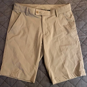 Beige golfshorts från Abacus W30 - Snygga beige golf shorts från Abacus i klassisk modell med två framfickor och två bakfickor. Tillverkade i ett stretchigt material av polyester och spandex för extra komfort. Perfekta för sommardagar och har bälteshällor för din favoritaccessoar.