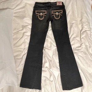 True Religion svarta bootcut jeans med glitter i strl 26 - Svarta jeans från True Religion med bootcut passform i storlek 26. Jeansen har lågmidja och bakfickorna är dekorerade med glittriga strassdetaljer och silverknappar. Klassisk femficksmodell i stretchig denim som ger en schysst siluett. Midjemått: 36 cm Plagget finns även upplagt på flera plattformar för att nå fler köpare, först till kvarn gäller. Tveka inte att höra av dig vid frågor!💕💕