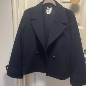 Svart skepparkavaj från Gina Tricot - Stilren marinblå  höstkappa från Gina Tricot med bred krage, guldknappar på ärmslut och framtill. Jackan har två fickor och är tillverkad i ett mjukt ull-liknande material. Perfekt för dig som gillar klassisk och clean look och en perfekt höstjacka❤️den är knappt använd och är som ny, slutsåld på hemsidan