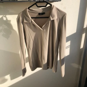 Beige ribbad långärmad tröja  - Snygg beige långärmad tröja med ribbad struktur och v-ringning med krage. Den är M men jag har S och har använt som oversize tröja jätte snyggt. Den är i tunn mjukt bomull