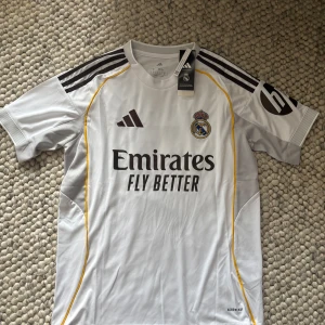 Real Madrid Vini Jr. 7 fotbollströja - Säljer en Real Madrid fotbollströja från Adidas med Vini Jr. och nummer 7 på ryggen. Tillverkad i lätt och ventilerande material med korta ärmar och Aeroready-teknologi. Den är lite stor i storleken så är du en mindre M kan den passa