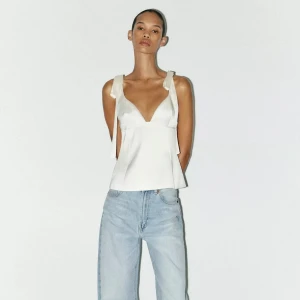 Vit satintopp med prislapp - Vit topp i satintyg med rosetter som knytningar ❤️‍🔥 Toppen är helt oanvänd och har prislapp kvar, säljer då jag beställde i två storlekar o sedan glömde lämna tillbaka den ena. Nypris 379kr, mitt pris 250kr 🤩