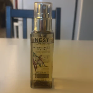 Nest Madagascar Vanilla Body Mist - Fräsch body mist från Nest i doften Madagascar Vanilla. Flaskan är fyrkantig och genomskinlig med guldig spraykork. Doften har inslag av vaniljstång, vaniljorkidé och kokos. Perfekt för dig som älskar söta och varma doftnoter. Flaskan rymmer ca 100 ml av 125.