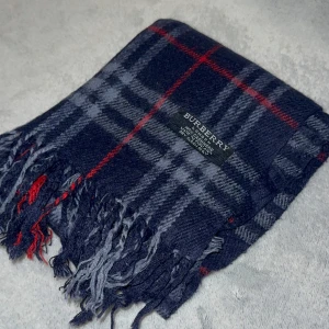 Rutig mörkblå halsduk från Burberry - Snygg halsduk från Burberry i mörkblått med klassiskt rutigt mönster i grått och röda detaljer. Gjord i 100% kashmir för en lyxig och mjuk känsla. Halsduken har fransar i ändarna och är perfekt för kalla dagar.