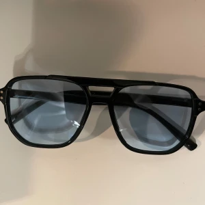 Tomford liknade glasögon - Snygga solglasögon med svart pilotformad båge och blåtonade glas. Klassisk design med markerad näsbrygga och breda skalmar. Perfekta för dig som vill ha en cool och tidlös look.