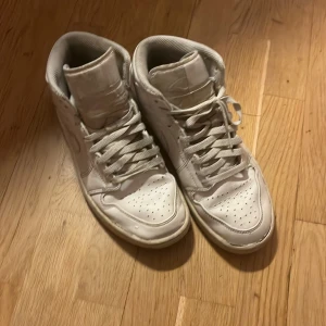 Nike Air Jordan 1 Mid Triple White - Säljer ett par Nike Air Jordan 1 Mid i helvitt skinn. Klassisk siluett med perforerad tå, snörning och ikoniska Swoosh-loggan på sidan. Diskret Air Jordan Wings-logo vid ankeln. Perfekta för dig som gillar clean och tidlös streetstyle. Nypris 1250