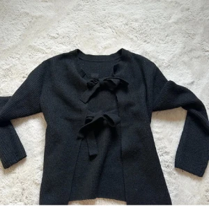 Svart stickad kofta med knyt - Trendig svart stickad kofta med croppad passform och långa ärmar. Koftan har snygga knytband framtill och baktill som ger en öppen känsla både fram och bak. Perfekt för dig som vill ha en unik och stilren look. 