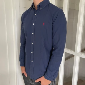 Polo Ralph lauren skjorta  - Säljer denna riktigt snygga mörkblåa Ralph lauren skjorta, den är i bra skick utan fläckar eller andra konstigheter, storlek M modell slim fit så den sitter riktigt snyggt, den är 73 cm lång och är 52 cm bred under armhålorna, jag på bilden är 183 cm för längdreferens, hör gärna av dig vid frågor!
