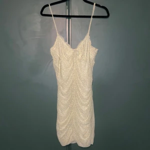 Blommig kortklänning från H&M Divided - Supersöt kortklänning från H&M Divided med smala axelband. Klänningen är ljusgul med små blommor i grönt och gult, har rynkade detaljer framtill och en liten knytning vid bysten. Perfekt för sommarens alla tillfällen!