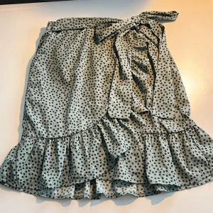 Prickig omlottkjol från ONLY XS - Sör ljusgrön kortkjol från ONLY i omlottmodell med svarta prickar, volangkant och knyt i midjan. 