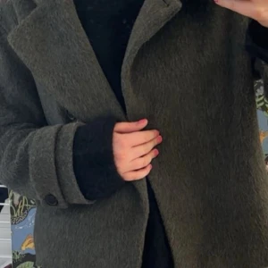 Grå ullkappa med bred krage - Snygg grå kappa i ull med bred krage och stora knappar vid ärmsluten. Klassisk och stilren modell som passar perfekt till lager-på-lager. Rak passform och långärmad design ger en cool och tidlös vibe.