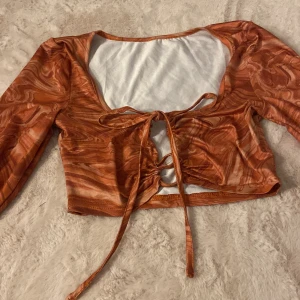Orange croppad topp med snörning - Säljer en croppad långärmad topp i orange med swirl-mönster. Storlek M