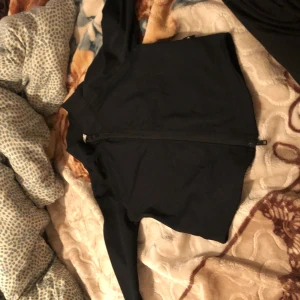 Svart sportig jacka från 157 - Svart, tunn och sportig jacka från 157 med hel dragkedja framtill. Jackan har en enkel design, lång ärm och är tillverkad i ett stretchigt syntetmaterial som passar perfekt för träning eller chill dagar. Snygg och clean look med liten krage.