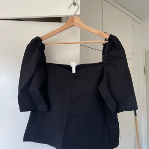 Svart offshoulder topp med puffärm - Säljer en svart offshoulder topp med trendiga puffärmar och rak skärning. Toppen har en stilren look med en hjärtformad halsringningen. Materialet känns mjukt och följsamt mot kroppen.