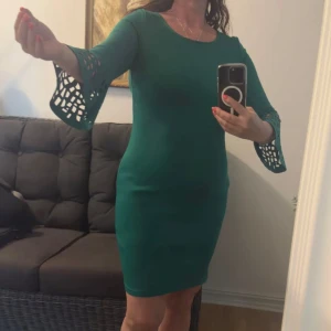Grön klänning från Bodyflirt Boutique - Snygg grön kortklänning från Bodyflirt Boutique med trekvartsärm och coola utskurna detaljer vid ärmsluten. Klänningen har en figurnära passform och rund halsringning. Perfekt för dig som vill sticka ut med en unik ärmdesign.