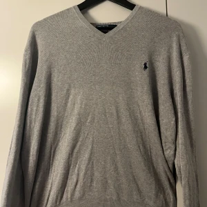Grå v-ringad tröja Polo Ralph Lauren - Klassisk grå v-ringad tröja från Polo Ralph Lauren i 100% pima bomull. Tröjan har lång ärm, ribbade muddar och den ikoniska broderade loggan på bröstet. Perfekt för en clean och stilren look. Nypris 2200kr