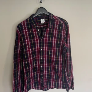 Rutig vinröd skjorta med knappar Boomerang - Snygg rutig skjorta i vinrött, blått och vitt med klassisk krage och knäppning framtill från Boomerang. Långärmad modell som passar perfekt till jeans eller chinos. Skjortan har en avslappnad passform och är tillverkad i mjuk bomull.