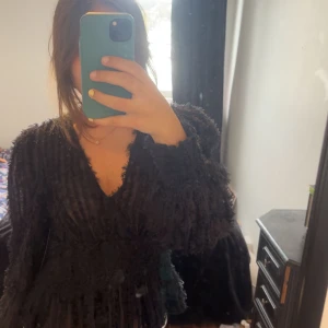 Svart fluffig blus från NA-KD - Supersnygg svart blus från NA-KD med fluffig textur och v-ringning. Långa ärmar och markerad midja ger en cool siluett. Inte använd, har prislapp kvar.