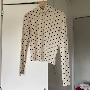 Prickig tröja - Beige mesh tröja med svarta prickar. Långärmad och tight passform, perfekt att styla med jeans eller kjol. Tunn och stretchig i syntetmaterial, med hög hals för en trendig look.