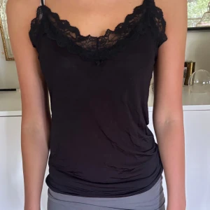 Svart spetstopp - Blank halvgenomskinlig med spetskant. Justerbara axelband.