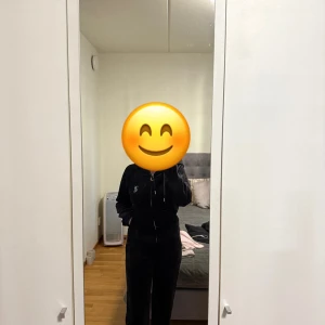 Svart velour hoodie från Juicy Couture - Svart hoodie i mjuk velour från Juicy Couture med dragkedja framtill, snörning i huvan och glittrig Juicy-text på ryggen. Långärmad och med fickor framtill. Perfekt för en chill och trendig look. Säljer byxorna i storlek S och koftan i storlek M.