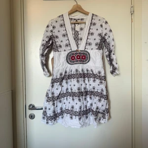 Odd molly klänning  - Unik kortklänning i vitt och broderade detaljer i brunt med coolt mönster.  Broderad detalj med röda blommor framtill. Djup v-ringning, markerad midja och trekvartsärm. Skön bomullskänsla och boho-vibe, perfekt för dig som gillar statement-plagg. Från märket Odd Molly i storlek 2 som enligt deras storleksguide motsvarar en storlek M. Mycket fint skick, jag hittar inga synlig anmärkningar eller defekter. 