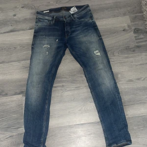 Blå slitna jeans från Levis - Säljer ett par blå jeans från Levis med snygga slitningar och lätt tvättad look. Klassisk femficksmodell med raka ben och normal passform. Perfekta för dig som gillar en avslappnad och trendig stil.