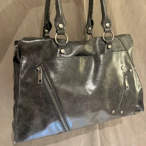 Svart axelväska i skinn med dragkedjor - Cool svart axelväska i skinnimitation med två rejäla handtag och snygga silverfärgade metalldetaljer. Den är 20cm höjd och 40cm bred!!💖Lite sliten i matrialet men dragkedjor och allt funkar!!🩷🩷