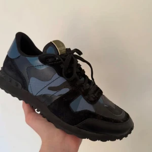 Valentino Rockrunner sneakers blå/svart - Snygga Valentino Rockrunner sneakers i blått och svart med coolt camouflagemönster. Skorna har detaljer i mocka och skinn, samt svarta snören och en robust sula. Perfekta för dig som vill sticka ut med stilrena och trendiga sneakers.