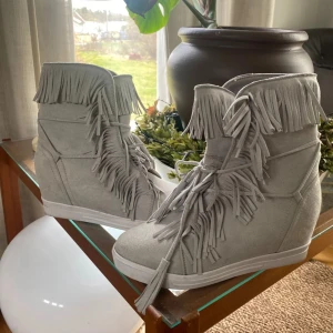 Grå mockasneakers med fransar och kilklack - Snygga grå sneakers i mocka med coola fransdetaljer längs skaftet och framtill. 