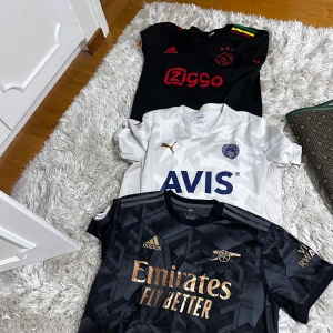 Tre fotbollströjor: Arsenal, Ajax, Fernerbache  - 200krr/styck. Säljer tre snygga fotbollströjor: svart Arsenal med guldtryck från Adidas, svart Ajax med röda detaljer och Ziggo-logga, samt vit FC Köpenhamn från Puma med diskret mönster och blå AVIS-tryck. Alla är kortärmade och har klubbmärken på bröstet. 