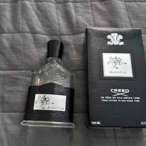 Creed Aventus 100ml Eau de Parfum - Lyxig parfym från Creed, Aventus 100ml. Flaskan är genomskinlig med svart och silverdetaljer, svart kork och elegant etikett med ryttare. Kommer i svart kartong med silverlogga och text. Perfekt för dig som gillar exklusiva dofter.