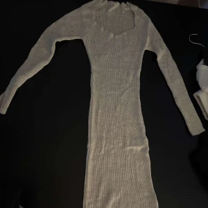 Beige ribbad långklänning - Snygg beige långklänning med ribbad struktur och lång ärm. Klänningen har en v-ringad hals och sitter tight mot kroppen för en smickrande siluett. Den har en slits där bak, säljer den då den är för liten och aldrig kommit till användning.
