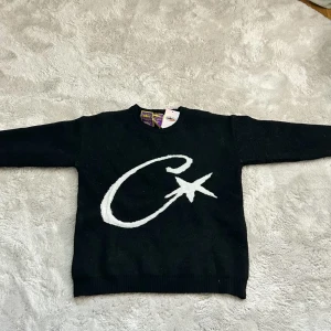 Svart stickad tröja från Corteiz - Säljer svart stickad tröja från märket Corteiz med stor vit C och stjärna på bröstet. Liten broderad logga på ärmen. Klassisk rund halsringning och långa ärmar. Använd ett fåtal gånger cirka 3-5 gånger. Storlek S men stor i modellen så känns som M!