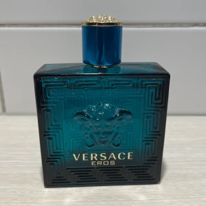 Versace Eros - Versace Eros är en ikonisk herrparfym i en stilren turkosblå glasflaska med Medusa-huvud och guldiga detaljer. Doften har inslag av vanilj, aromatiska och gröna toner, samt fräsch citrus, trä och sötma. Flaskan har en lyxig och modern design som sticker ut i badrumshyllan.